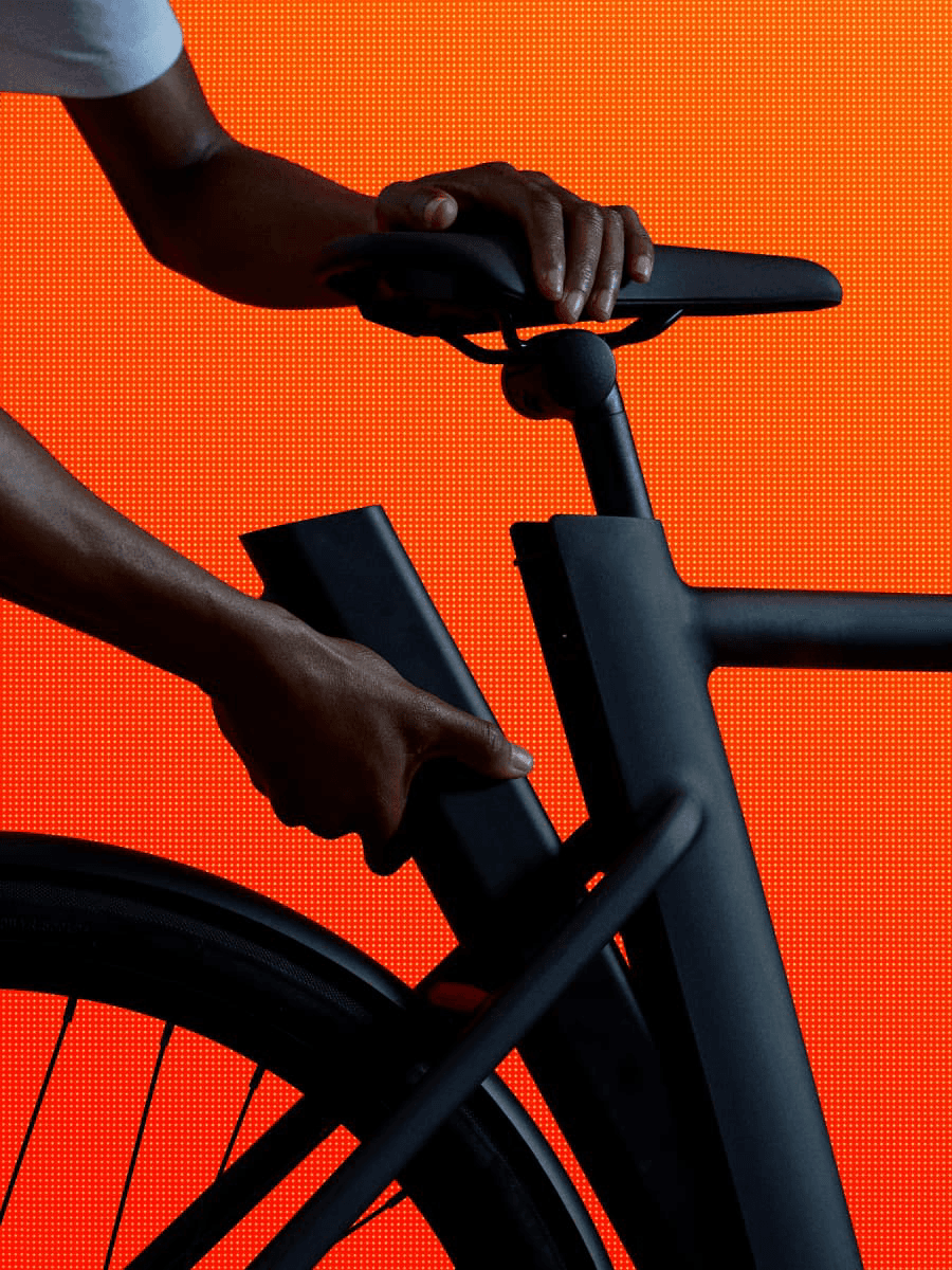 A hand on the handlebar of a black e-bike against an orange background.