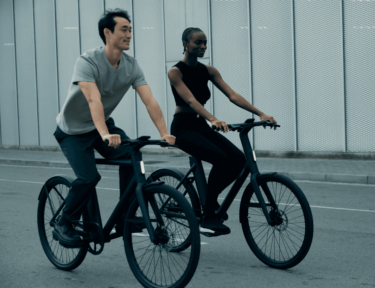 Two people riding e-bikes along a street.